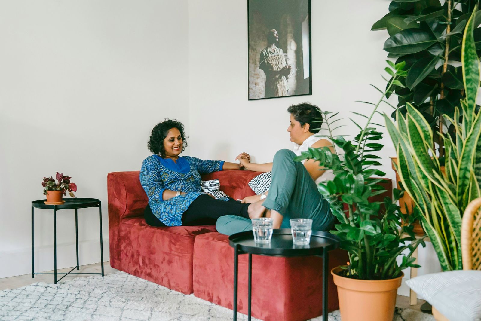 Two women sitting together on a sofa in a bright living room, talking